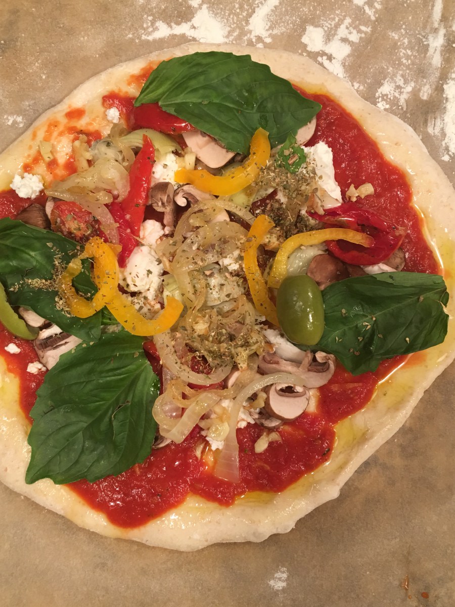 Unbaked pizza with sauce, mushrooms, peppers, olives, spinach, onions, and goat cheese